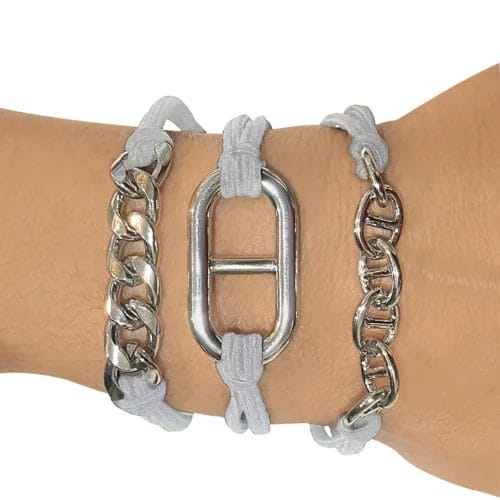 A wrist wearing three Maya J bracelet hair ties with gray elastic hair bands and silver colored links in three different shaped styles.