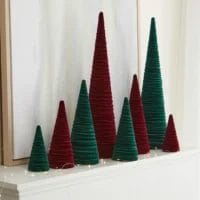 Three sizes of Velvet Christmas Trees line a white mantle. The trees are simple cone shapes wrapped in velvet material and are shown in two colors- a deep emerald green and a bright red.