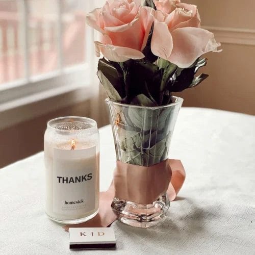 Thanks candle lit sitting next to a bouquet of pink roses as an example of a thank you gift