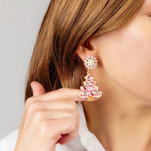A hand pushes out a Rhinestone Christmas Tree Earring hanging from an earlobe.