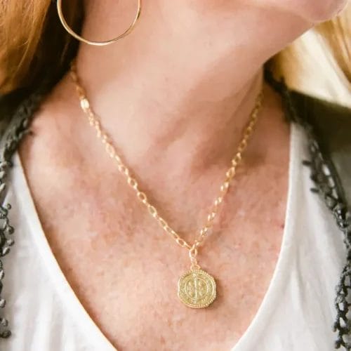 The St Benedict gold coin necklace is showcased on a model's neck.