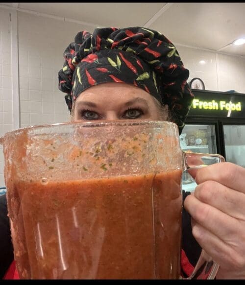 Woman hides behind large blender of salsa.